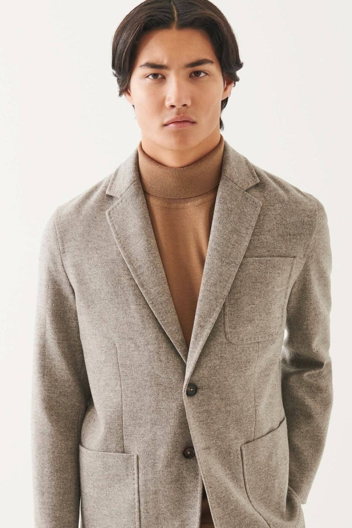 Blazer en laine à deux boutons, couleur gris, porté par un homme avec un col roulé beige.