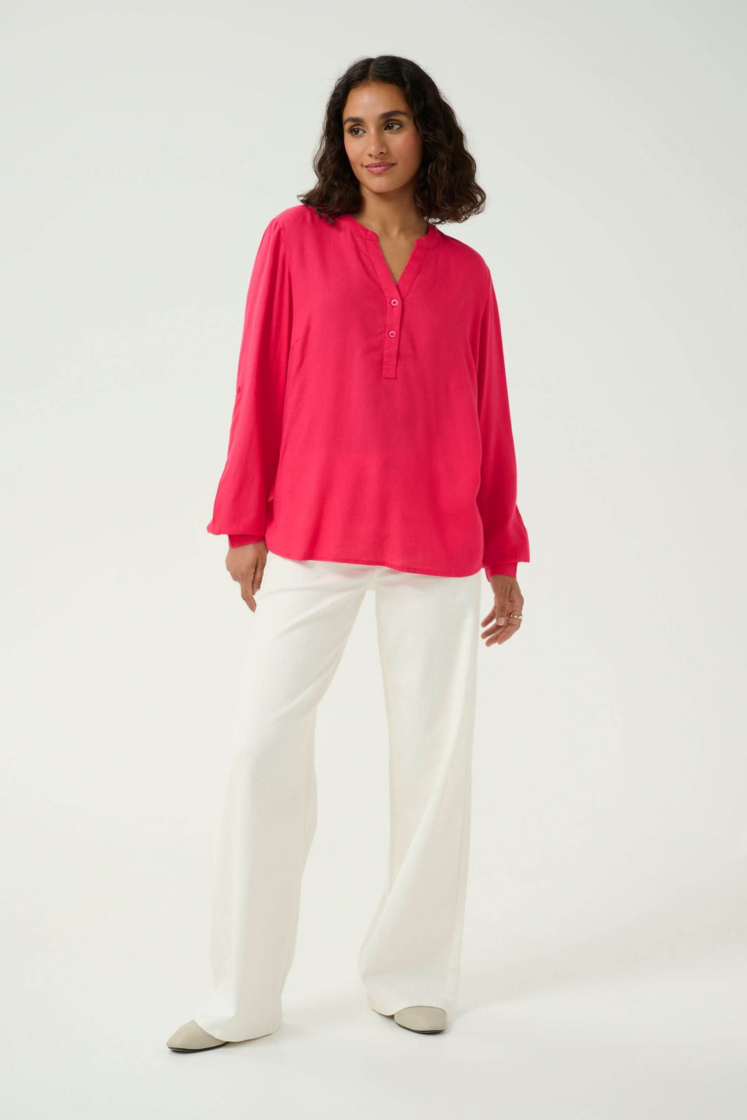 Blouse Milia rose fluide à col tunisien, manches retroussables, portée avec pantalon blanc.