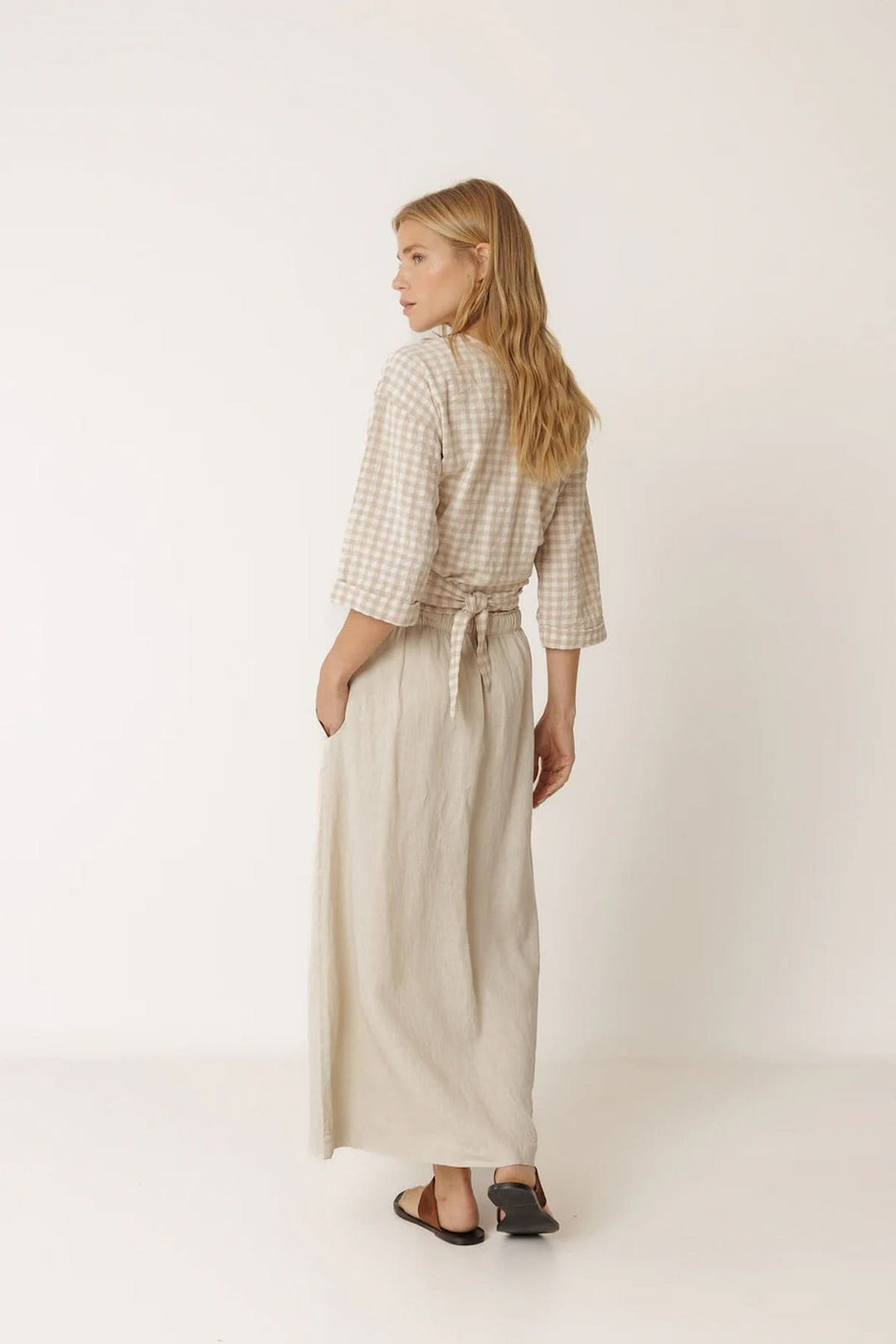 Femme portant une blouse cache-cœur à motif vichy avec manches 3/4 et encolure croisée, vue de dos.