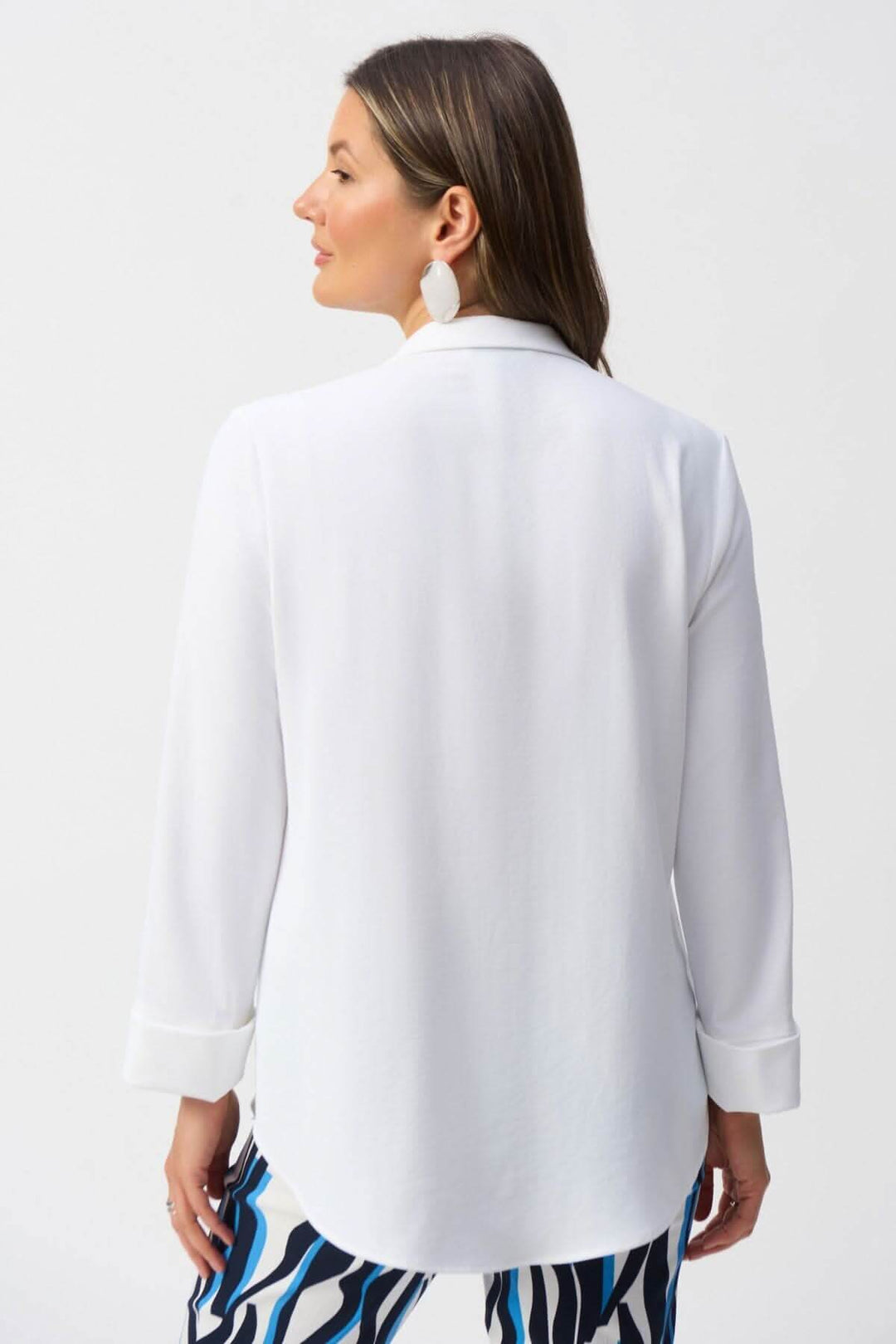Femme portant une blouse classique blanche, vue de dos, avec col en V et manches longues. Élégance raffinée.