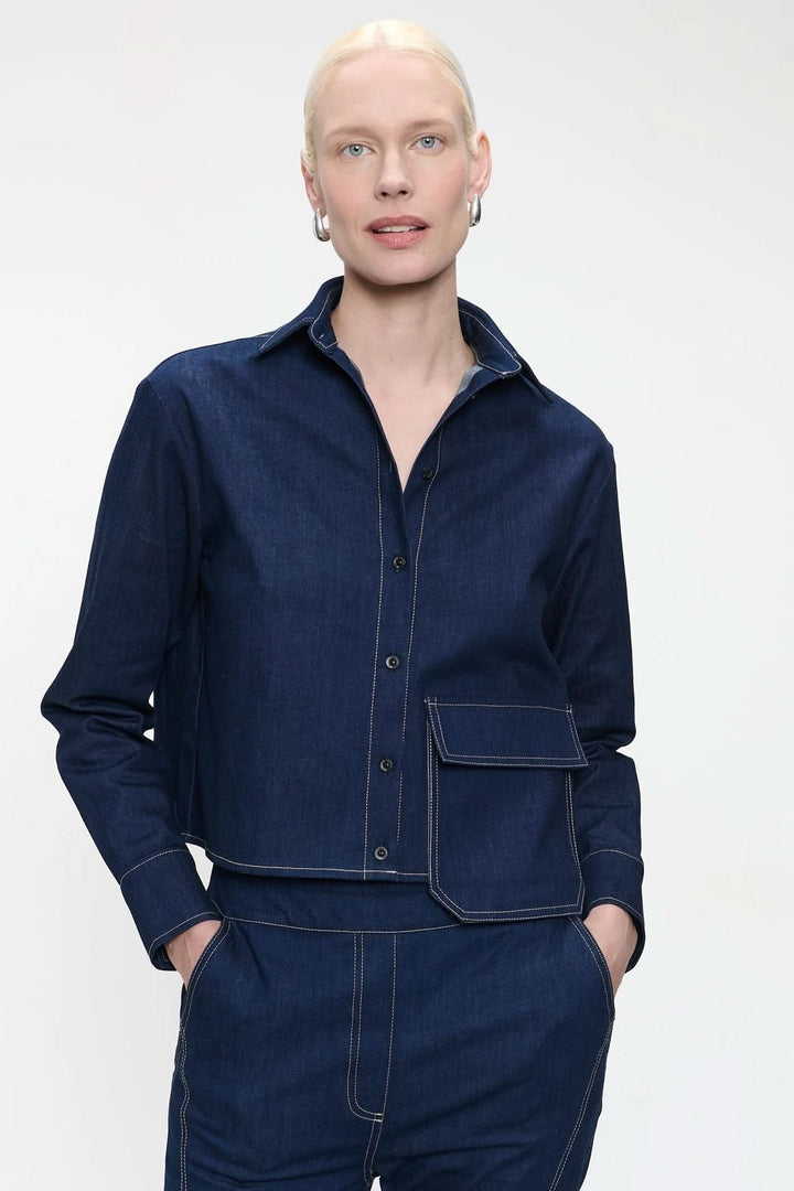 Blouse en denim avec grand rabat de poche et surpiqûres contrastantes, style utilitaire moderne.