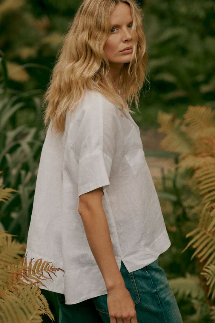 Blouse en lin à manches chauve-souris portée par une femme en extérieur, idéale pour un look estival élégant et décontracté.