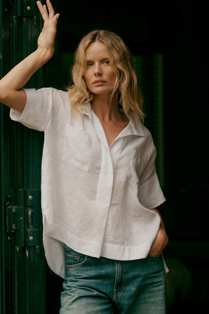 Modèle portant une blouse en lin à manches chauve-souris, coupe ample, col chemise ouvert et jean.