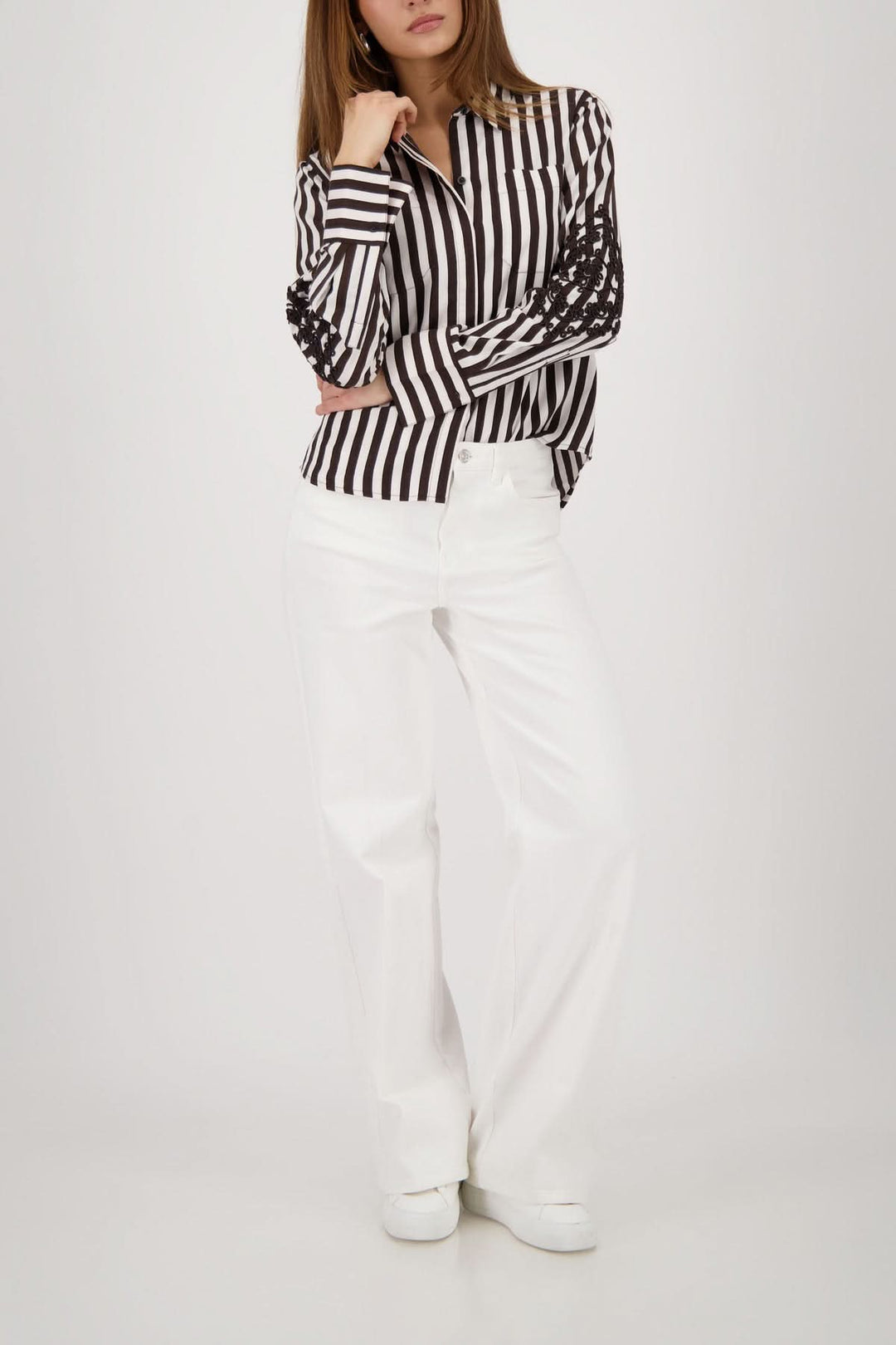 Blouse rayée avec broderies aux manches portée avec un pantalon blanc, vue de face. Motif rayé vertical et broderies sur les manches.
