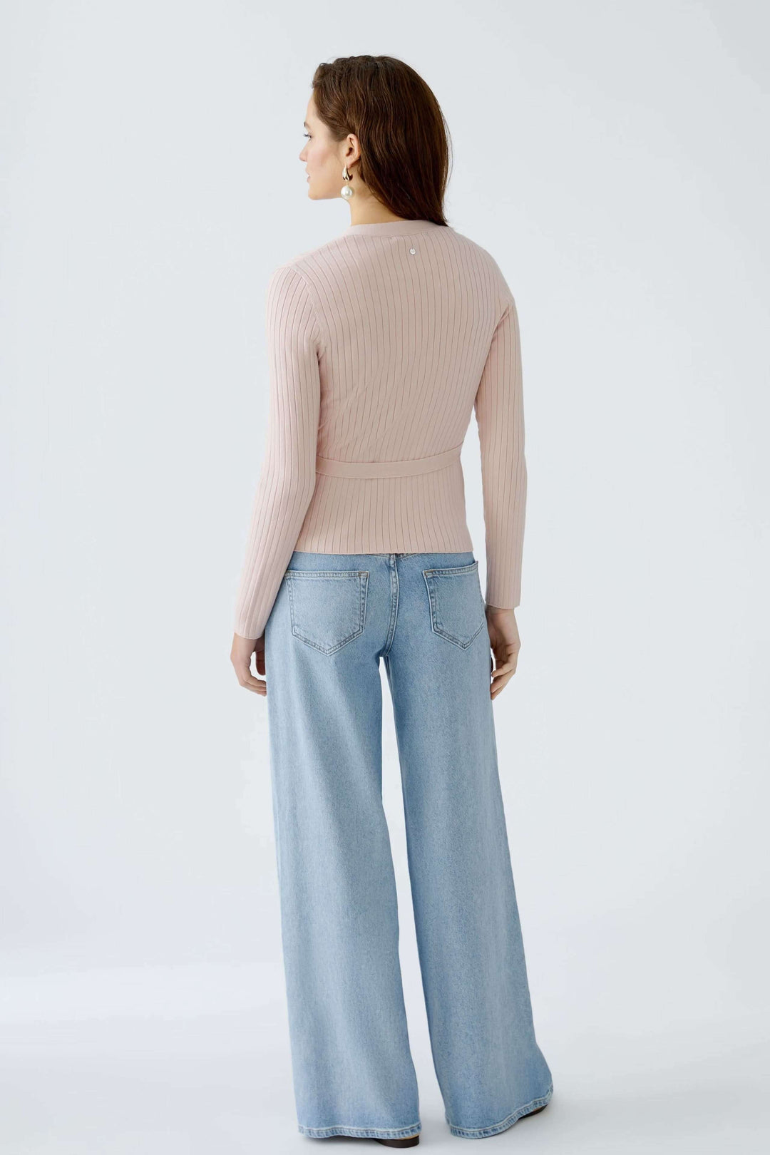Femme vue de dos portant un cache-cœur en maille rose avec un pantalon en denim large.