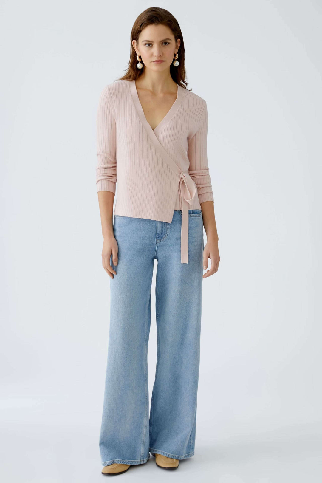 Cache-cœur en maille rose avec liens à la taille et manches longues, porté avec un pantalon large en denim.