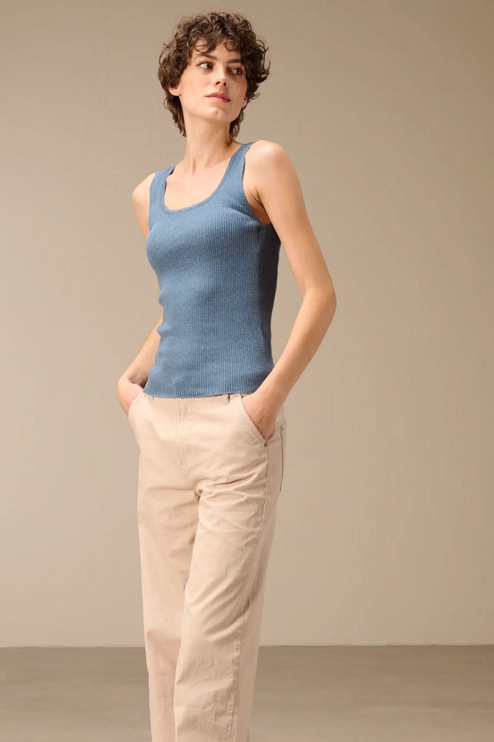 Femme portant une camisole côtelée ajustée col rond bleue, associée à un pantalon beige, mettant en valeur une tenue décontractée et élégante.