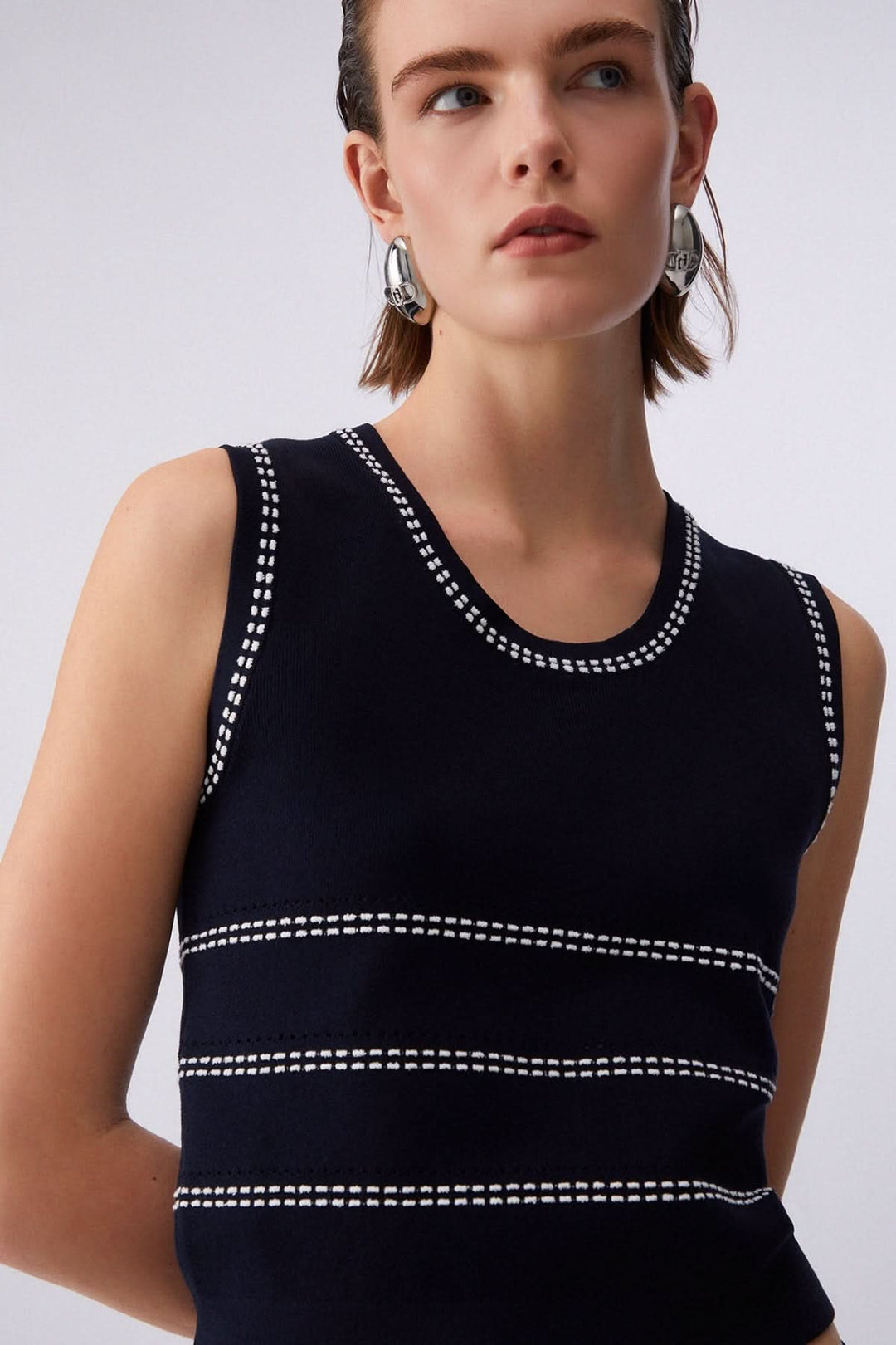 Femme portant une camisole en maille sans manches à motif rayé élégant, encolure ronde, coupe moderne.