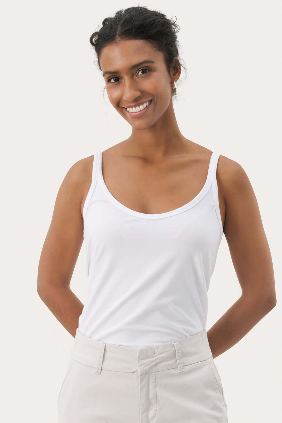 Femme portant une camisole à encolure arrondie blanche avec bretelles fines, design épuré pour élégance et confort.