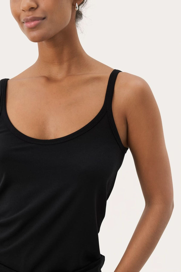 Femme portant une camisole à encolure arrondie noire avec bretelles fines et look élégant et confortable.