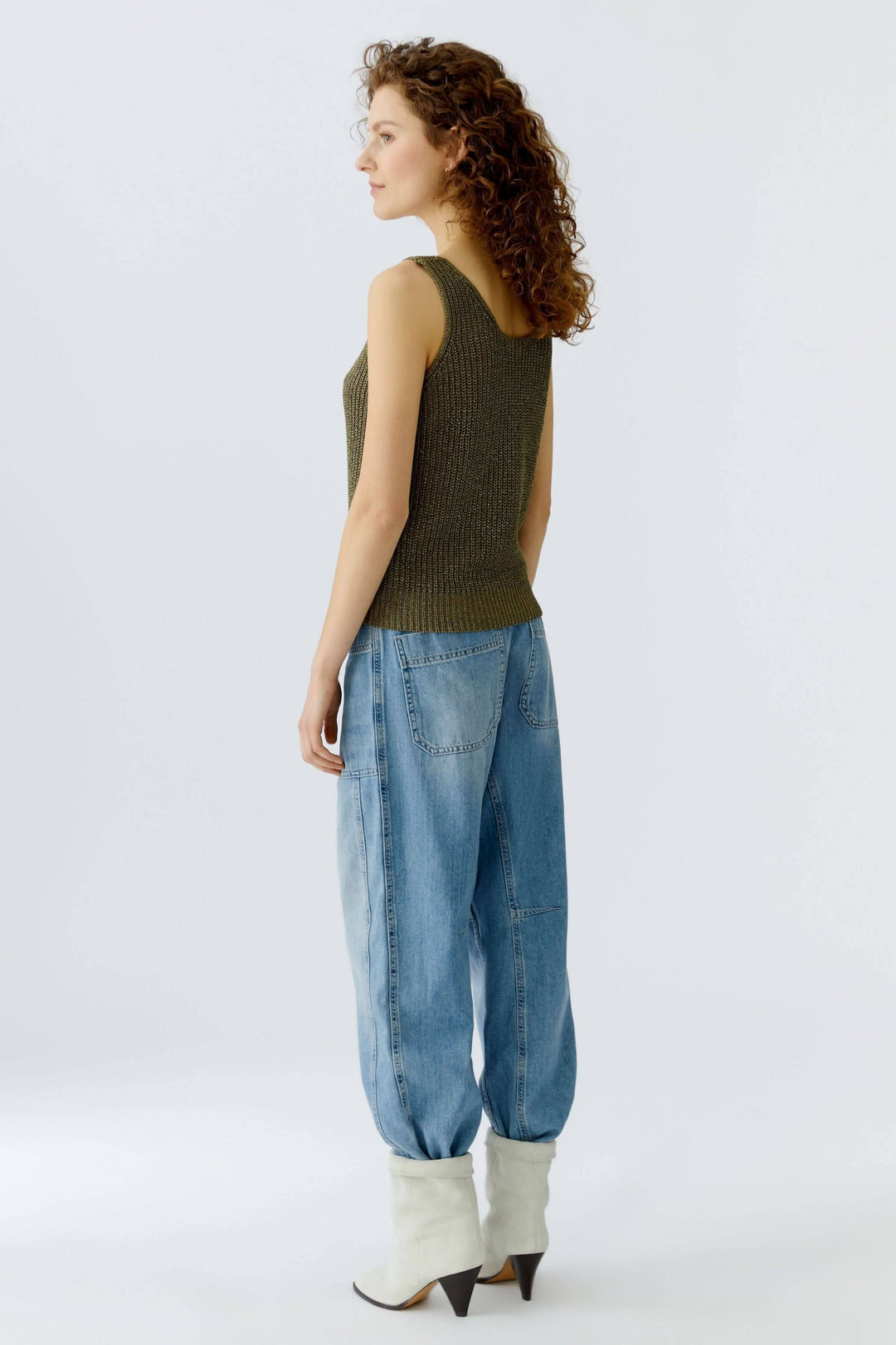 Femme portant une camisole tricoté en fil spécial verte, avec un jean ample et des bottines, vue de profil.