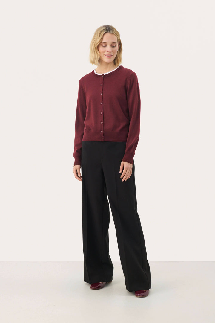 Cardigan Noelani classique à encolure ronde, porté avec un pantalon noir, idéal pour un look de bureau ou décontracté.