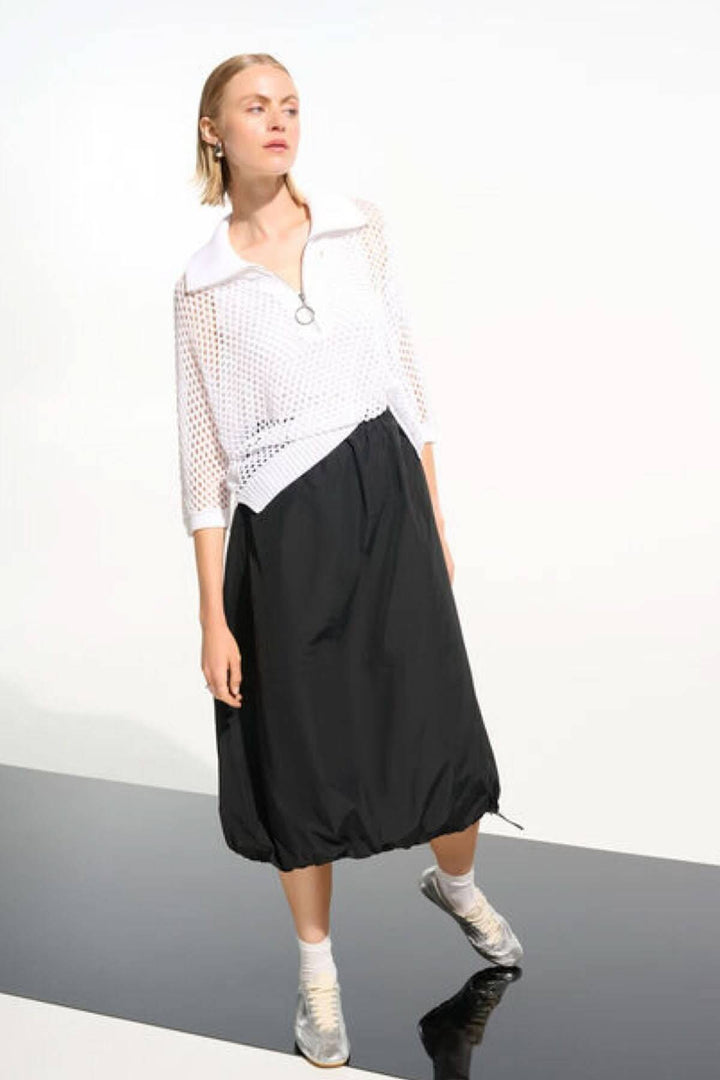 Femme portant un chandail ajouré à col zippé, style moderne et léger avec une jupe noire. Mode élégante et polyvalente.