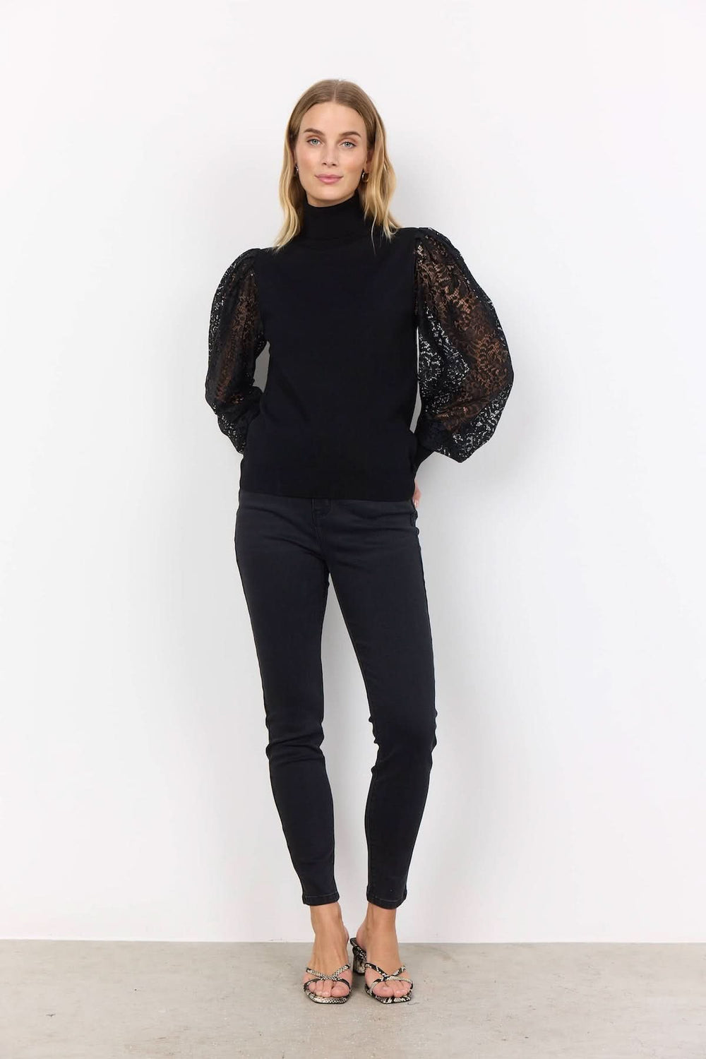 Chandail à col montant noir avec manches en dentelle transparente pour un style chic et féminin.