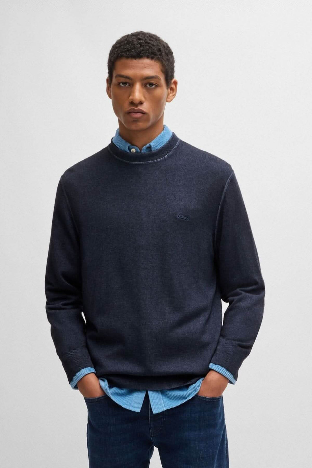 Homme portant un chandail col rond en laine, associé à une chemise bleu clair, style décontracté.