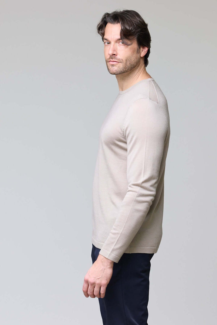 Homme portant un chandail col rond en tricot fin beige, texture douce, coupe ajustée et manches longues, style élégant et raffiné.