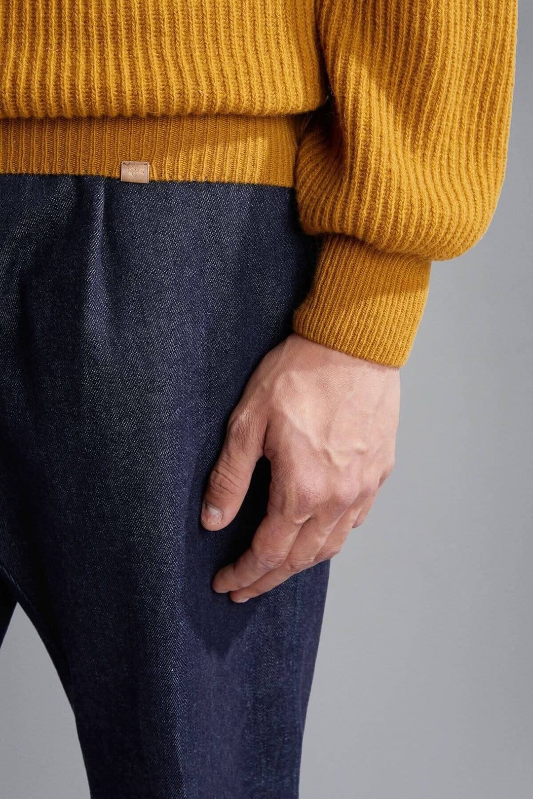Chandail côtelé en laine jaune moutarde porté avec un pantalon en denim, logo discret de la marque apparents.