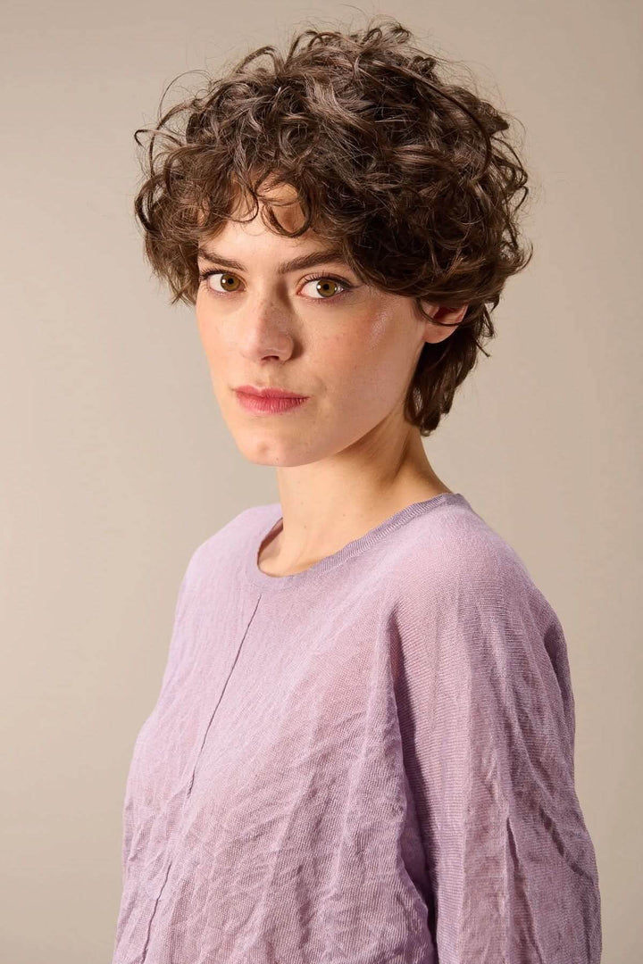 Femme portant un chandail en maille fine, couleur lavande, avec texture froissée et coupe droite, style moderne et décontracté.