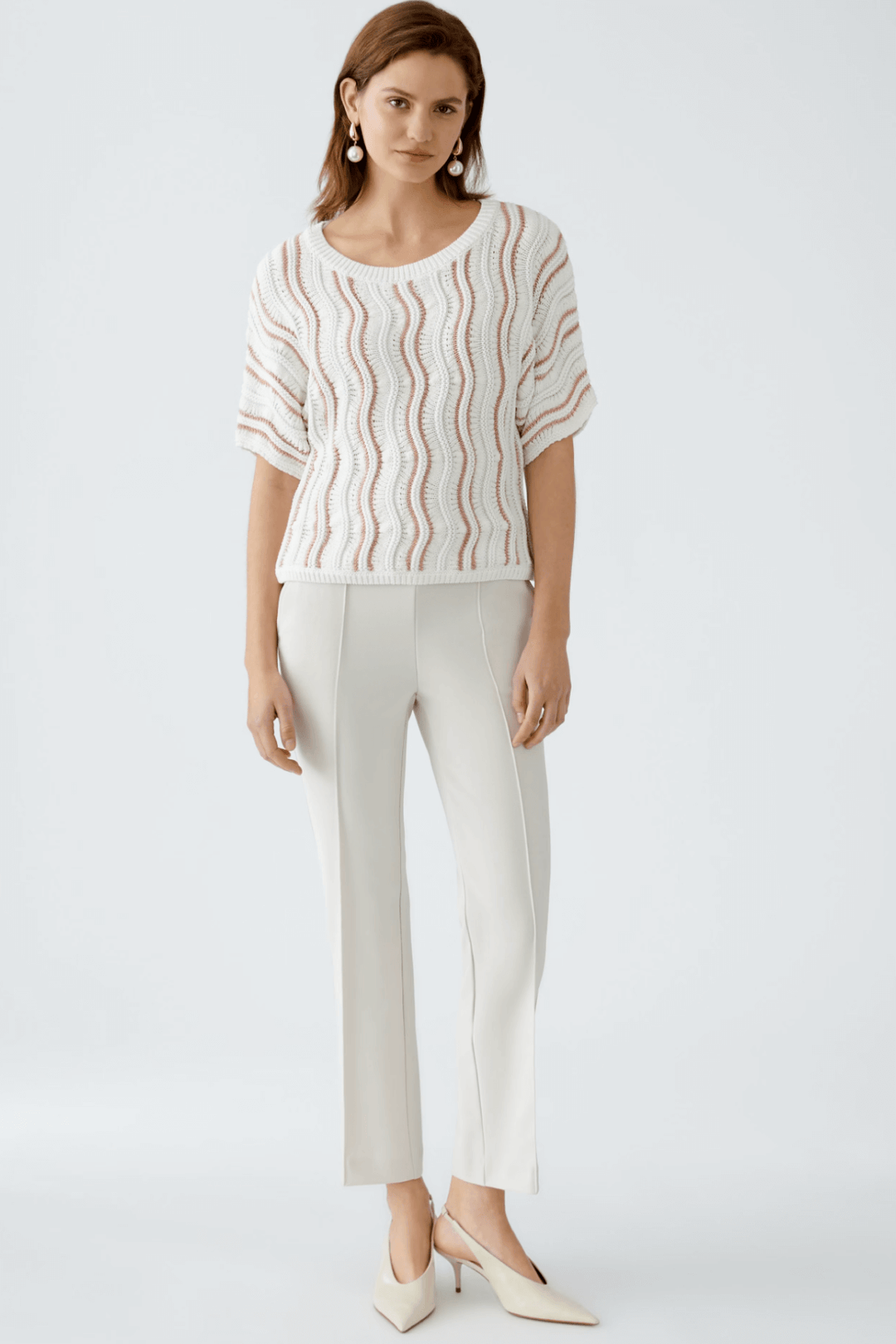 Femme portant un chandail en maille texturée avec motif ondulé et pantalon blanc, look décontracté et féminin.