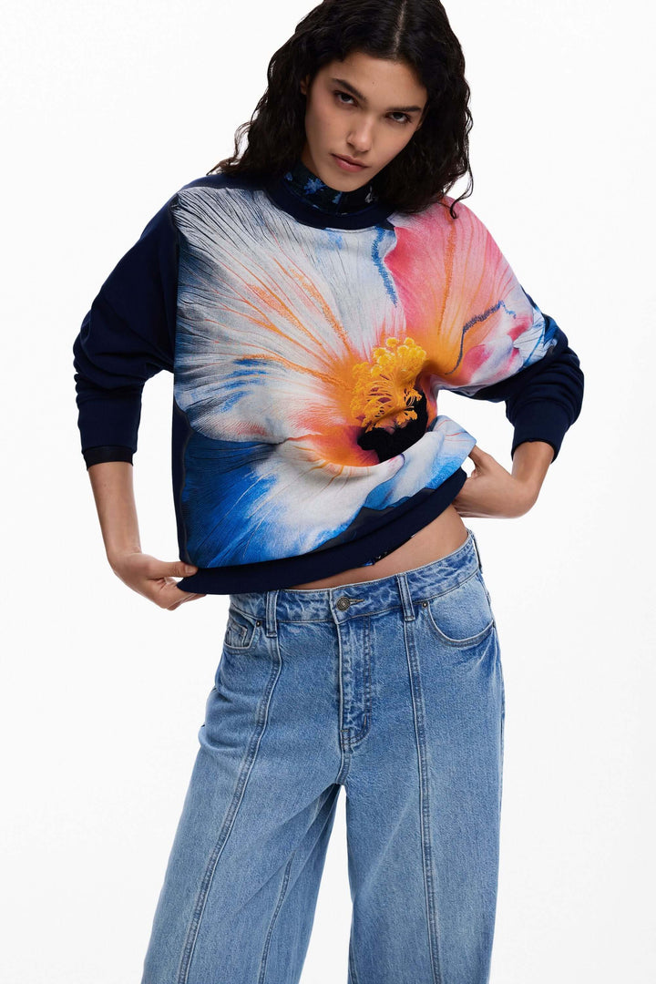 Chandail à grande fleur avec motif floral surdimensionné, porté avec un jean, offrant style et confort pour une tenue moderne.