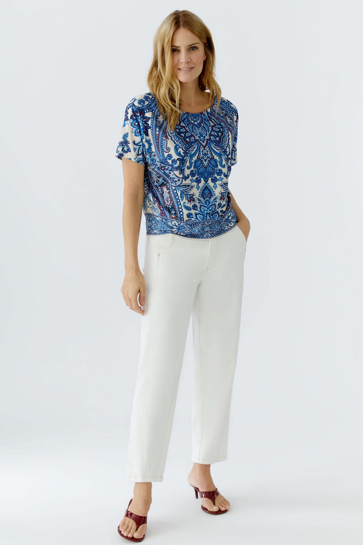 Chandail imprimé à manches courtes au motif cachemire, porté avec un pantalon blanc pour un look décontracté et raffiné.