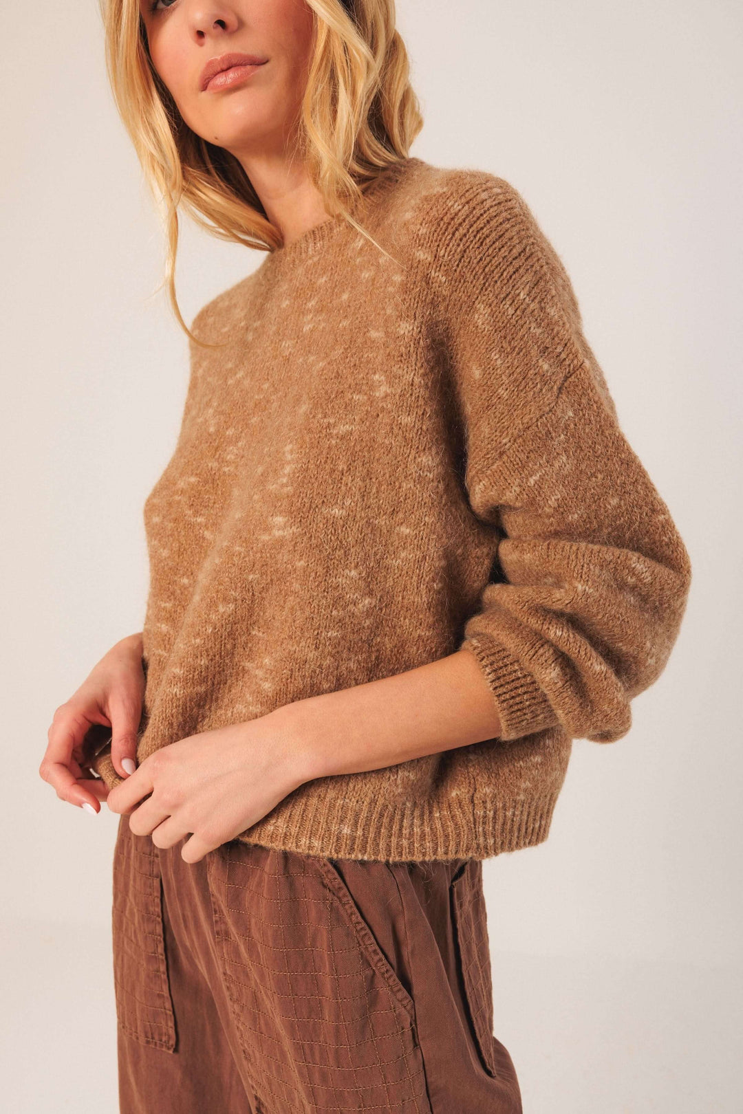 Femme portant un chandail maille texturée avec manches bouffantes, idéal pour un look décontracté et chaleureux en saison froide.