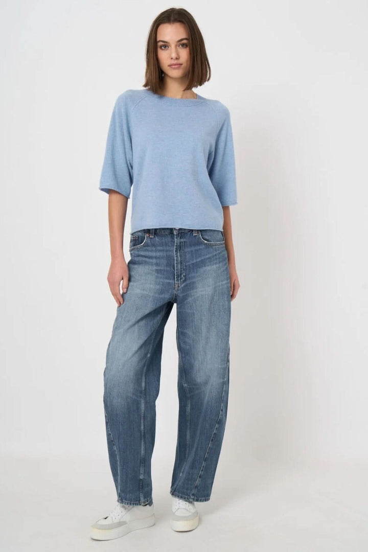 Femme portant un chandail à manches courtes bleu, coupe droite et encolure ronde, avec un jean décontracté et des baskets blanches.