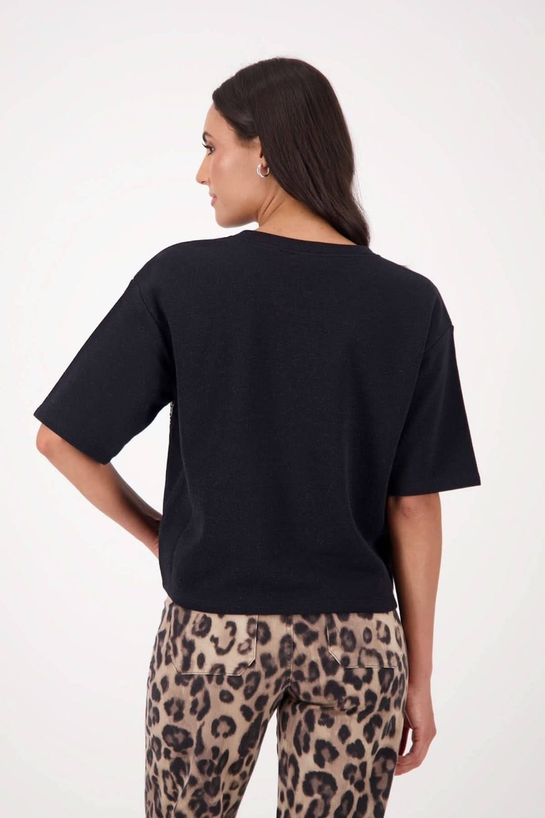 Femme portant un chandail à manches courtes noir avec des appliqués de paillettes, vue de dos, assorti à un pantalon imprimé léopard.