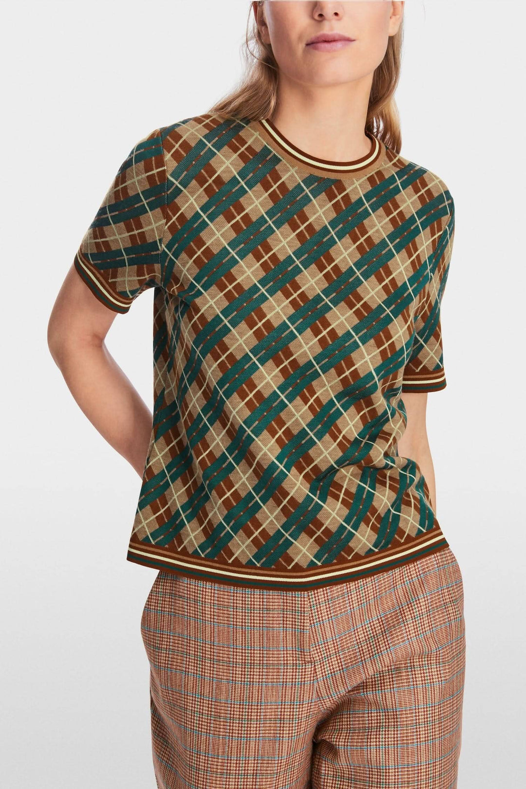 Chandail à motifs losanges en laine douce avec encolure ronde et manches courtes, porté avec un pantalon à carreaux.