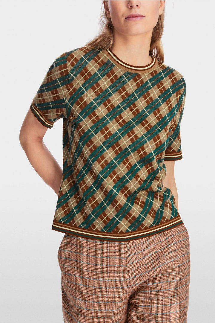 Chandail à motifs losanges en laine douce avec encolure ronde et manches courtes, porté avec un pantalon à carreaux.