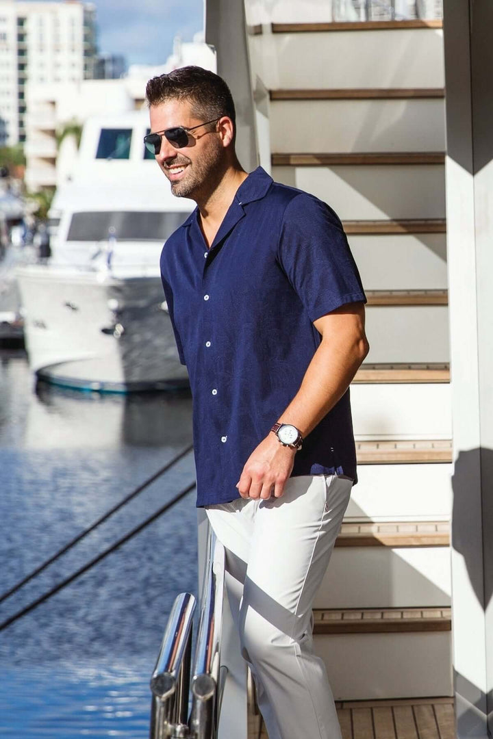 Homme portant une chemise à manches courtes bleu marine, lunettes de soleil, marchant au bord d&