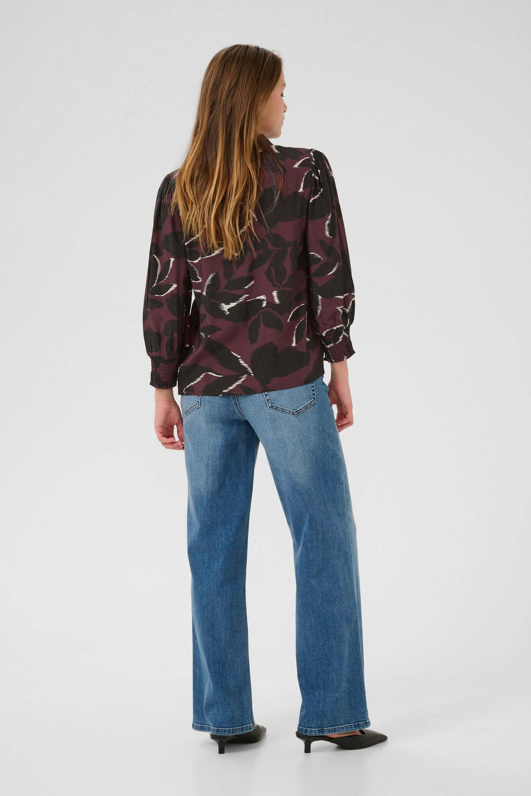 Femme portant la Chemise Mille imprimée avec des manches longues et un jean, vue de dos, style moderne et quotidien.