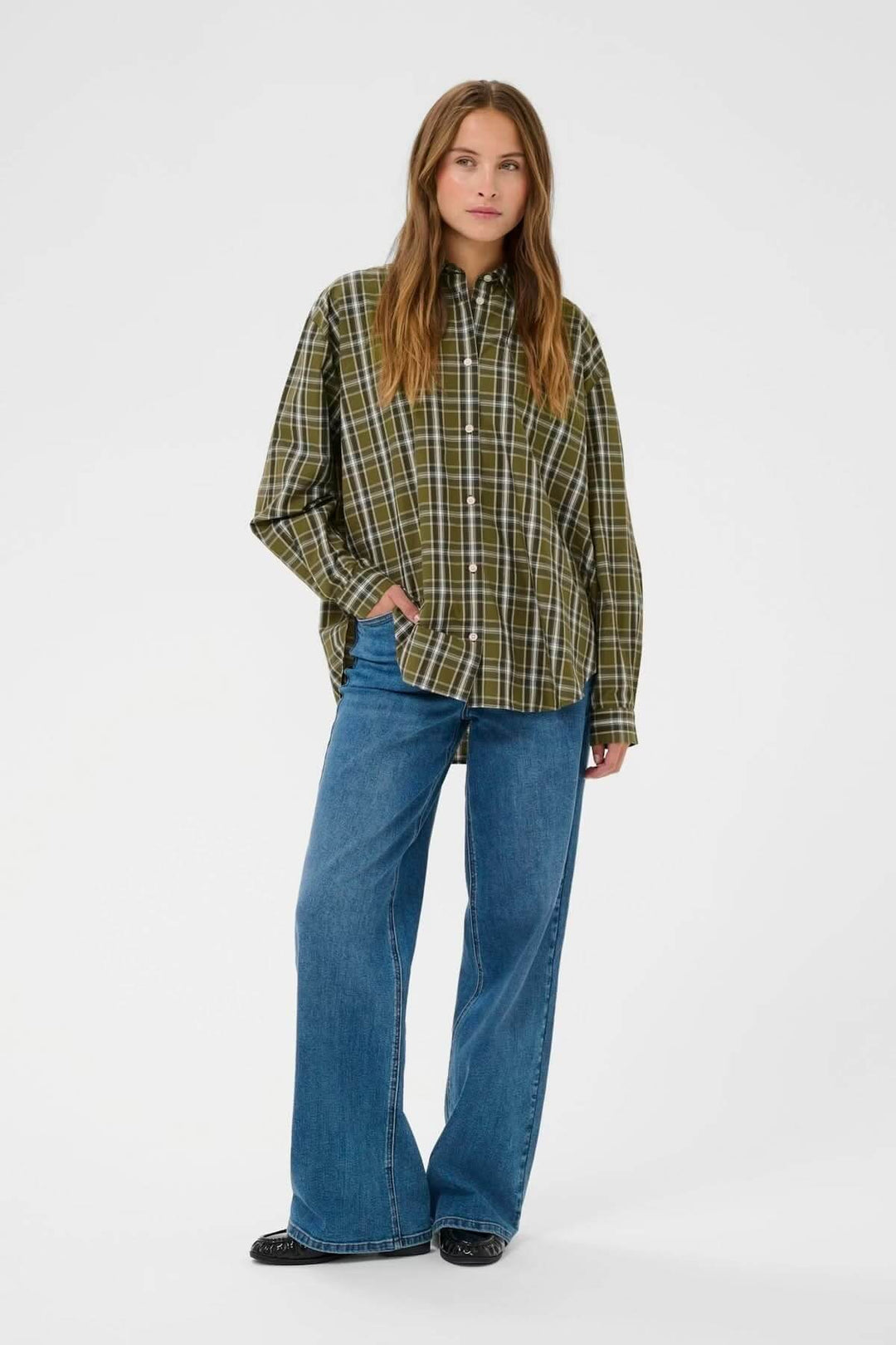 Femme portant une chemise à carreaux verte, coupe décontractée, avec un jeans évasé bleu pour un look casual chic.