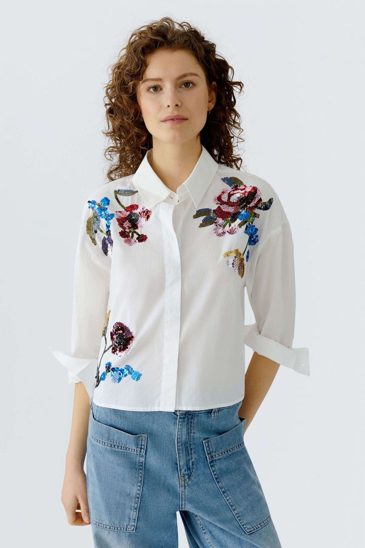 Femme portant une chemise coupe moderne avec des broderies florales, style élégant et décontracté.