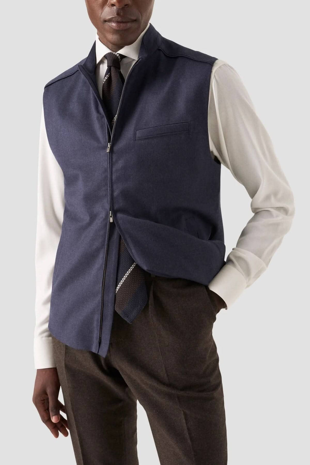 Homme portant un gilet bleu marine avec fermeture éclair, chemise blanche et cravate, style élégant.