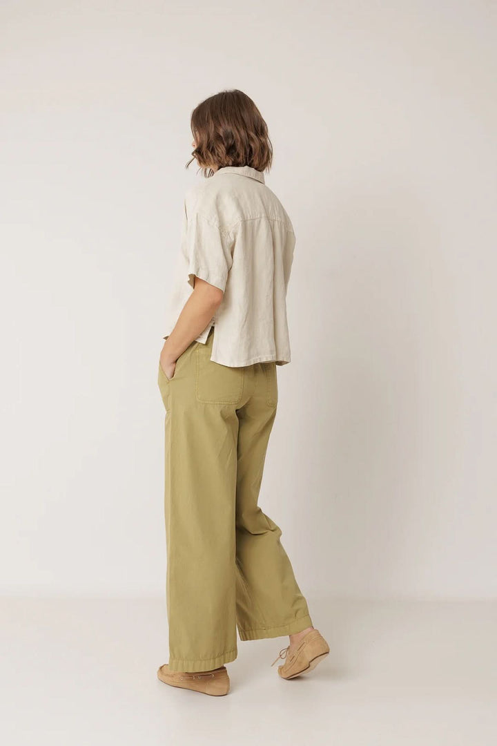 Femme portant une chemise en lin à coupe décontractée avec un pantalon olive, vue de dos, sur fond neutre.