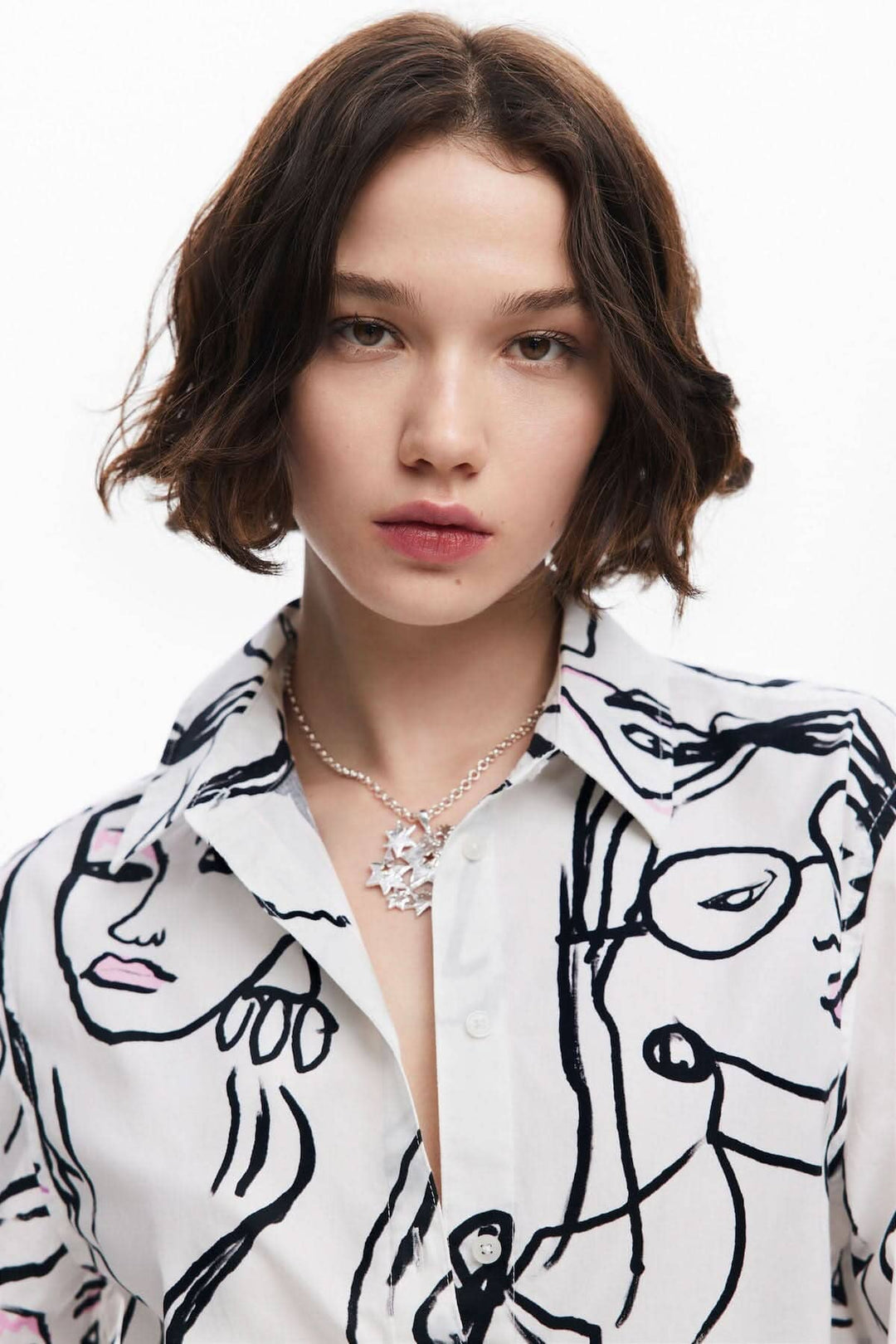 Chemise à imprimé visage, manches longues, portée avec un bijou élégant, style chic et moderne.