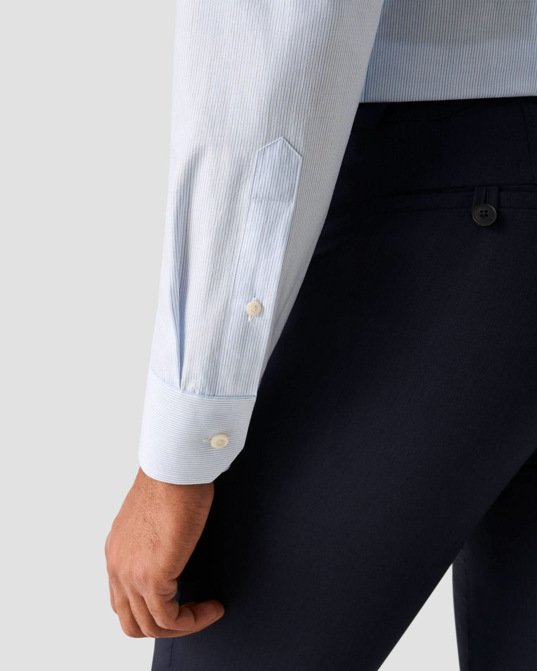 Détail de la chemise lignée bleue claire avec col blanc et manche ajustée.