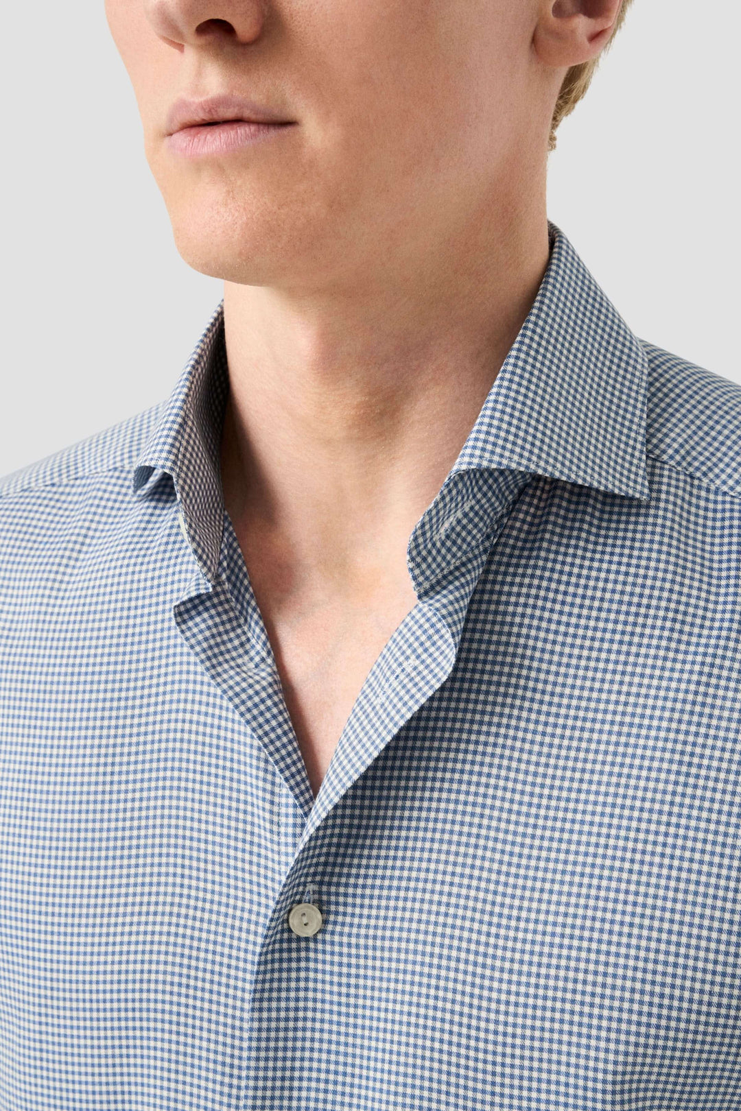 Homme portant une chemise motif carreaux avec col classique ouvert et boutons nacrés, style chic et moderne.