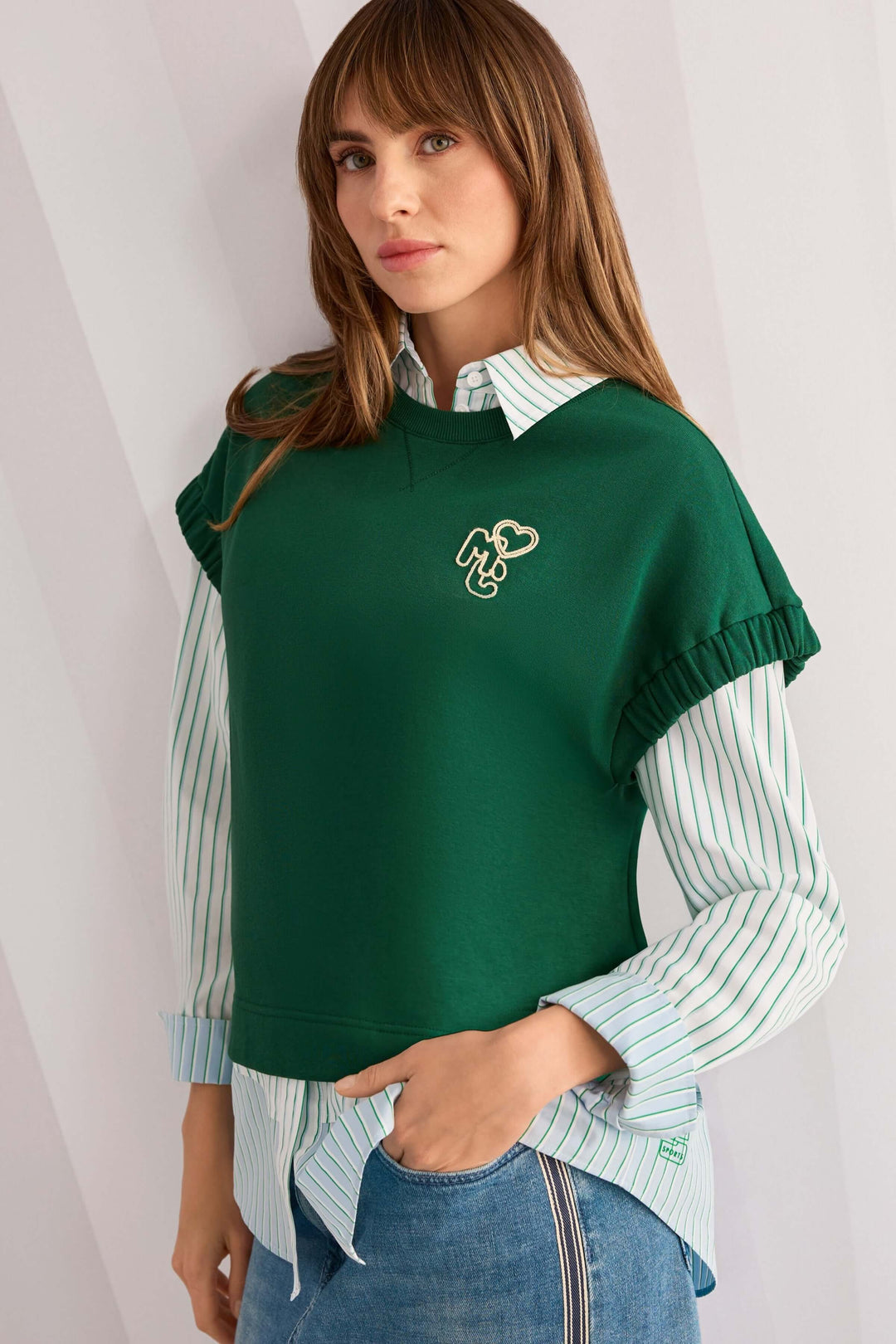 Femme portant une chemise rayée en coton sous un pull vert, look moderne et décontracté.