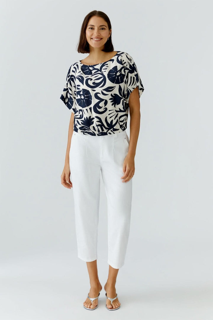 Femme portant un Chemisier à manches courtes imprimé artistique avec un pantalon blanc, coupe fluide et confortable.
