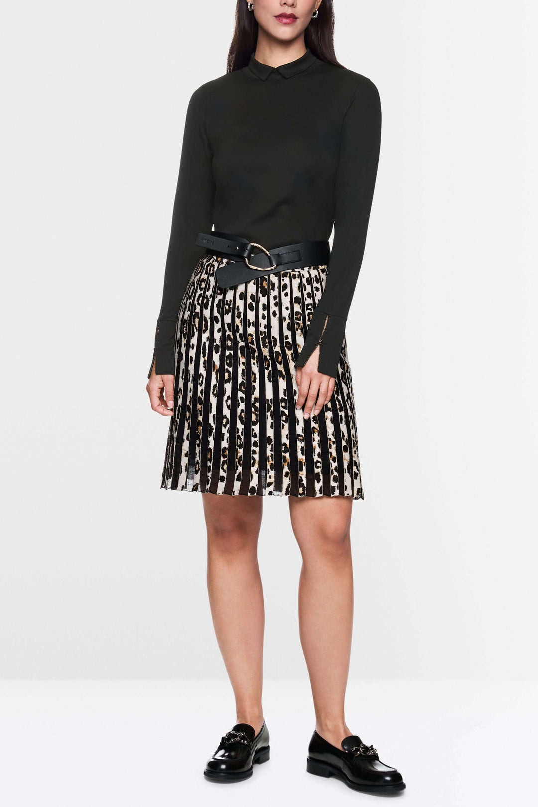 Col roulé ajusté noir avec col fendu et fermetures zippées, porté avec jupe plissée et ceinture large pour un look chic.