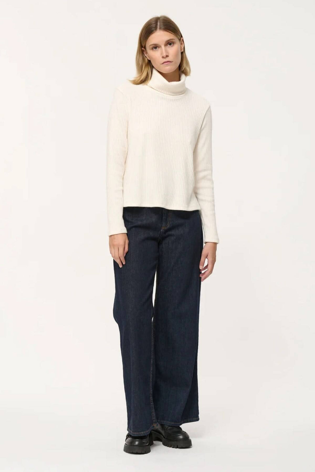Femme portant un col roulé côtelé blanc avec un jean ample, parfait pour un look élégant et décontracté.