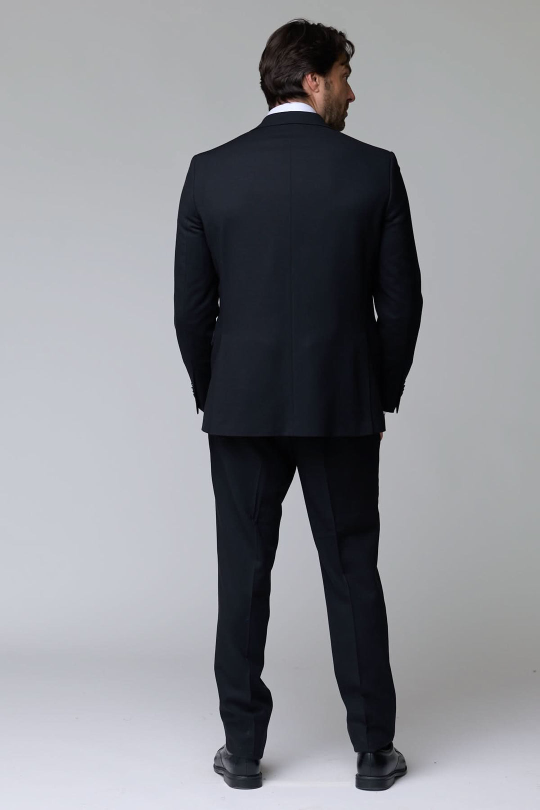 Homme portant un complet classique deux pièces noir, vue de dos, élégant pour le bureau et occasions formelles.