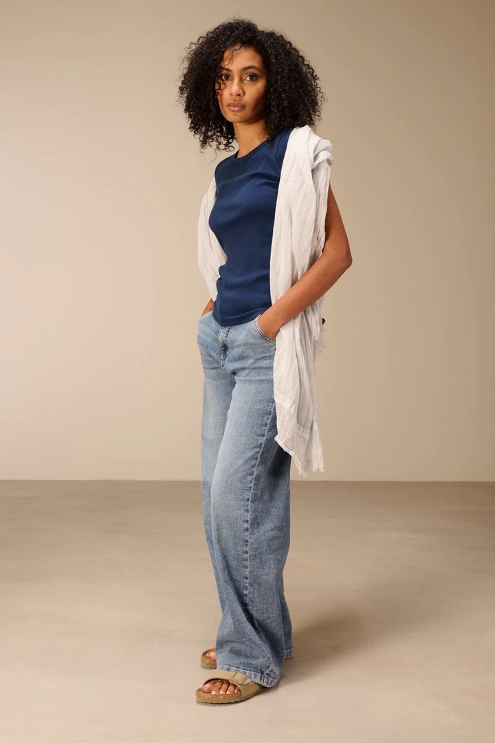 Modèle portant un foulard en coton blanc fluide et léger, combiné avec un haut bleu et un jean, affichant un style décontracté et élégant.