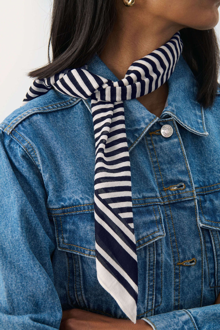 Foulard Phi aux motifs rayés porté autour du cou avec une veste en jean, parfait pour une touche élégante.