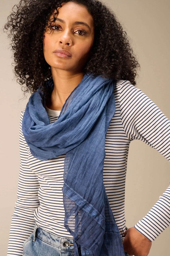 Foulard en coton bleu porté sur un pull rayé, montrant sa texture fluide et élégante.