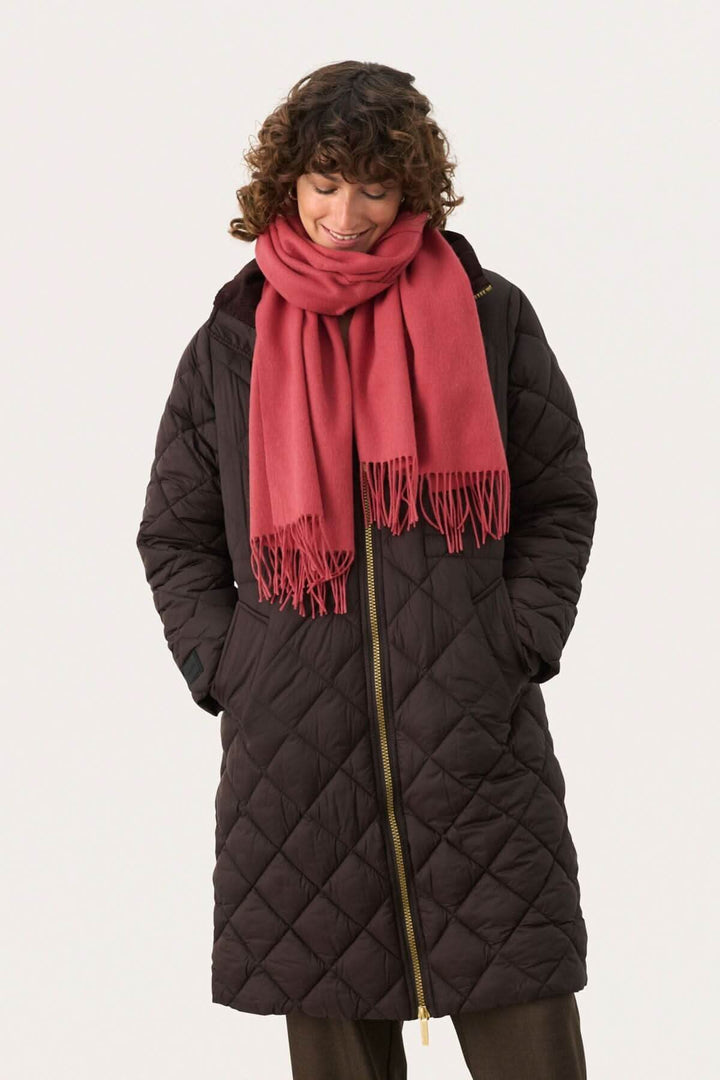 Femme portant une doudoune noire et un foulard en laine rose, souriante et élégante pour l&