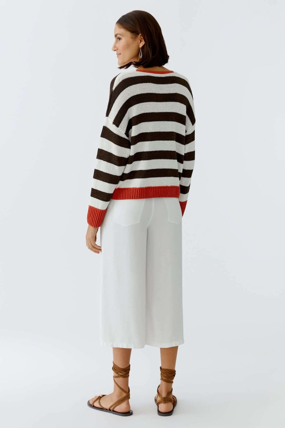 Derrière d'un modèle portant un haut tricot rayures modernes avec des pantalons blancs et des sandales élégantes.