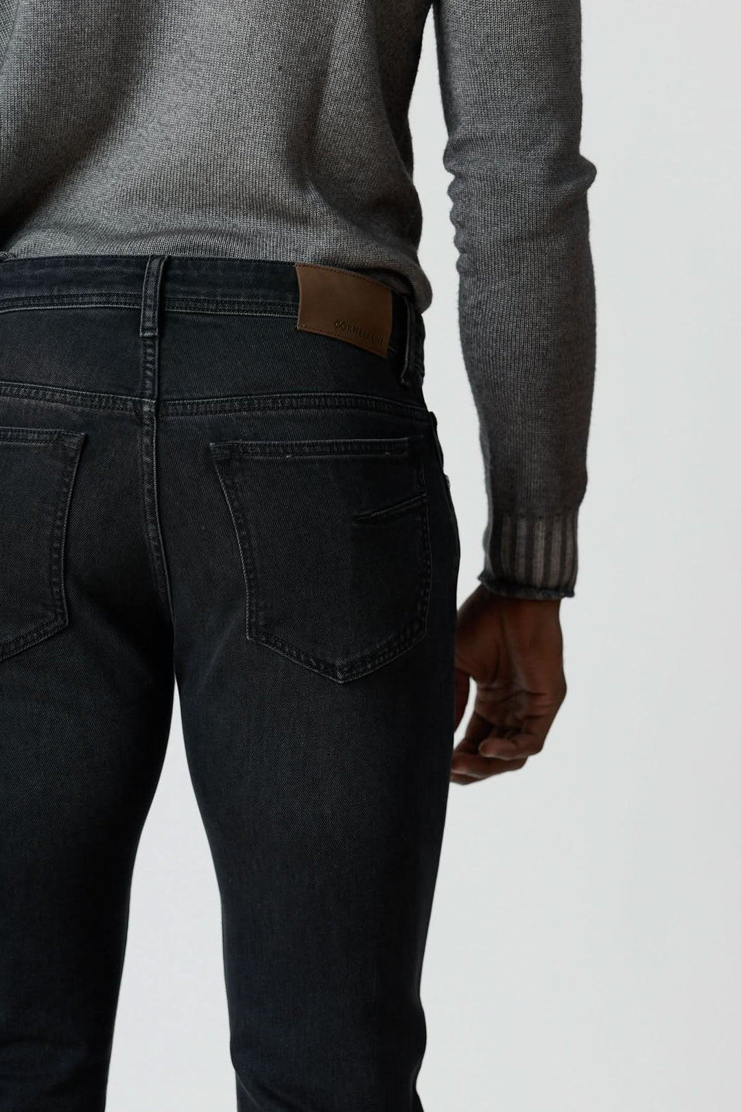Jean 5 poches en denim stretch gris foncé avec silhouette ajustée, vue arrière, porté avec pull gris.
